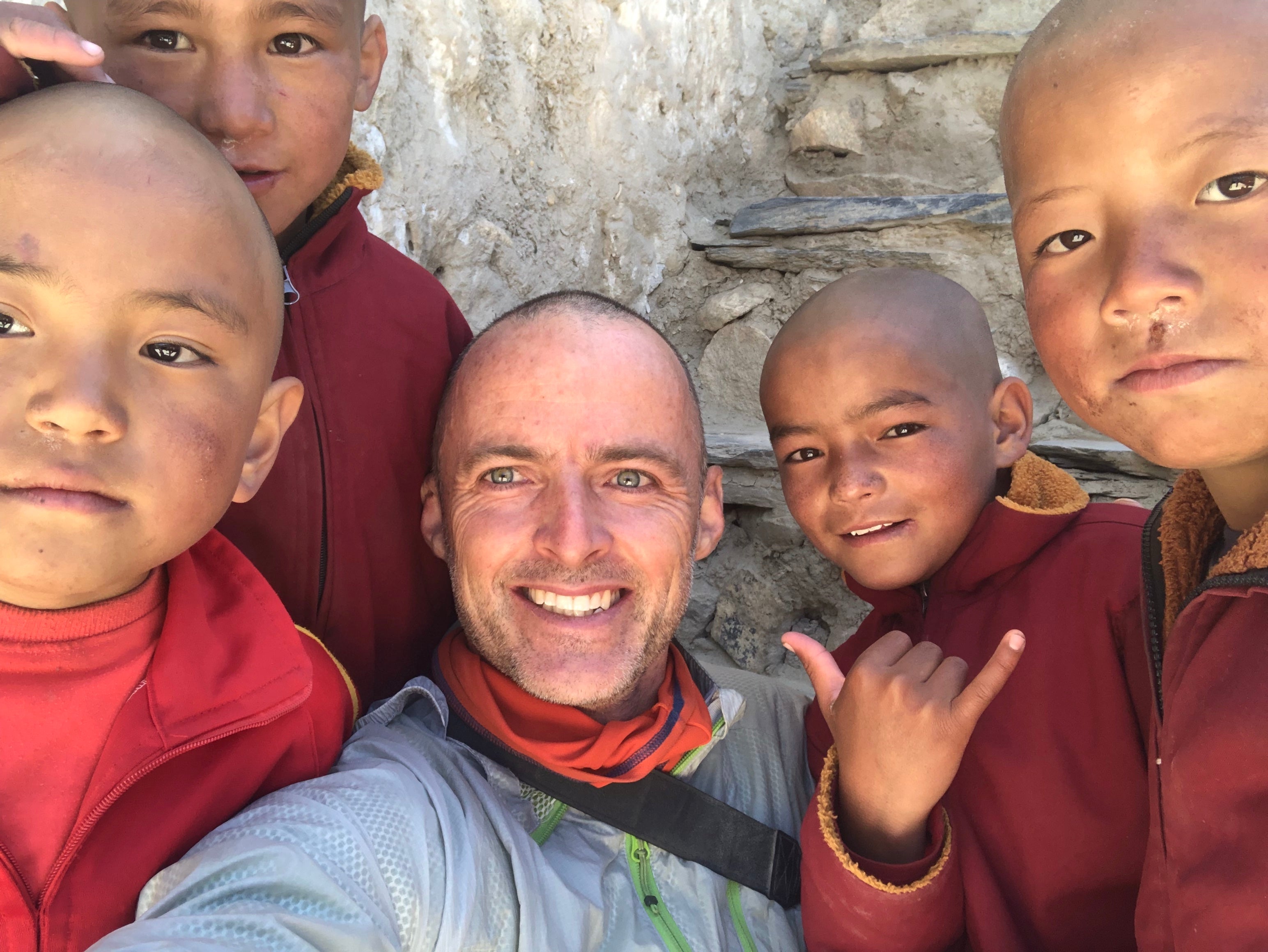 Photo of the author Alan Riva with 4 young smiling buddhist monks at a monastery in upper mustang in nepal.